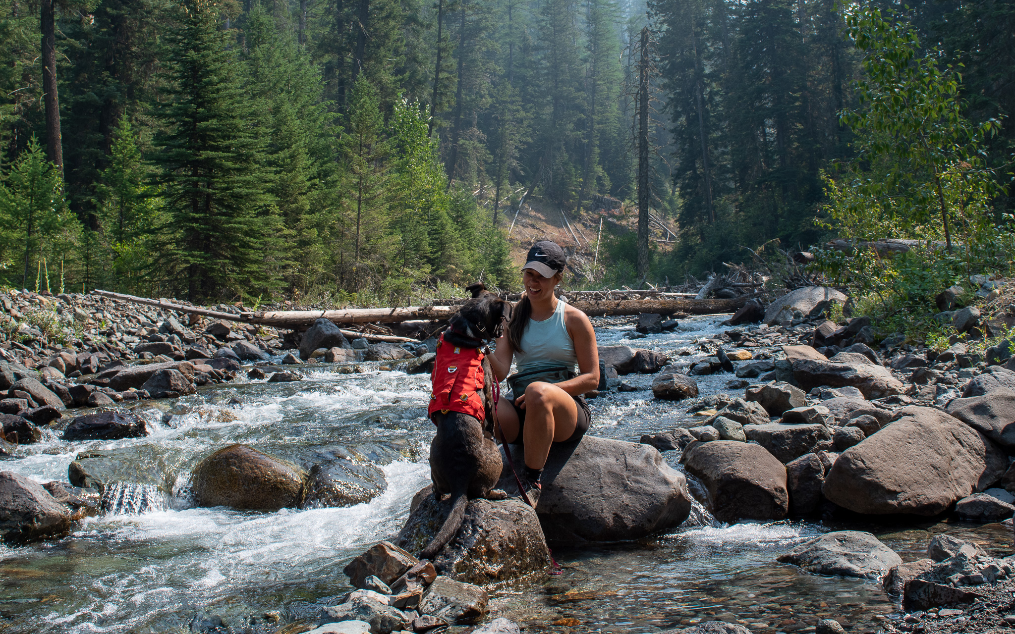 Mia and her dog Zella sitting on some rocks along a river in the Wallowa Mountains